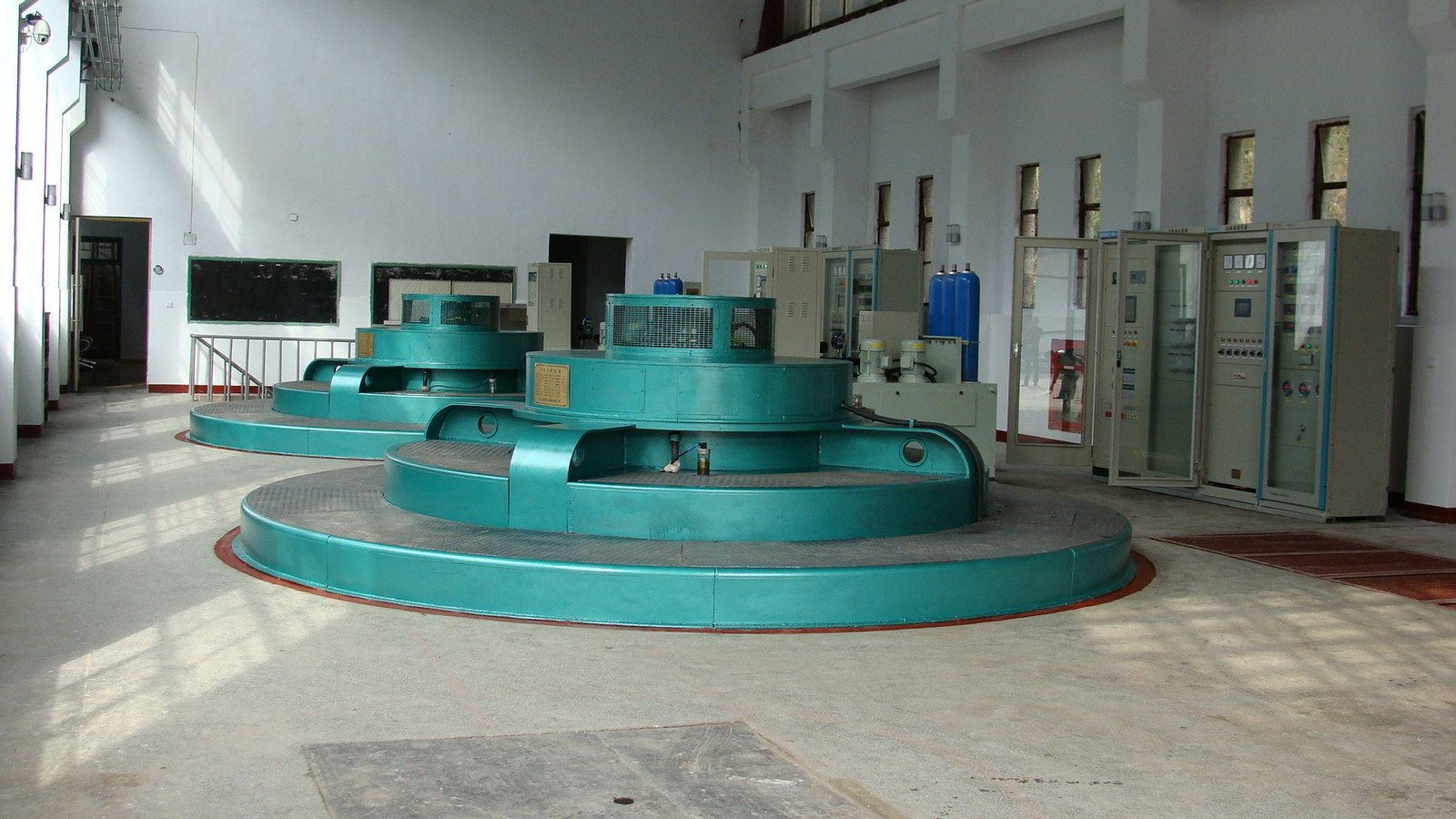 Two vertical turbine-generator units with a row of control panels at Fengle hydropower plant