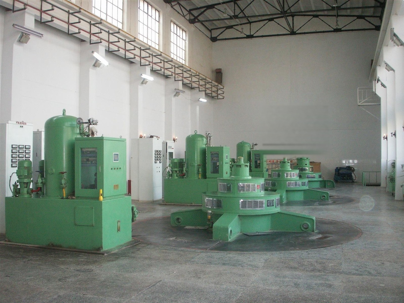 Row of vertical turbine-generator units with pressure oil tank and governor cabinet at Wukushake hydropower plant